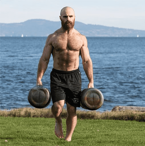 Lucas Parker Crossfit athlete farmer's carries weights outside by the sea whilst doing crossfit grunt work