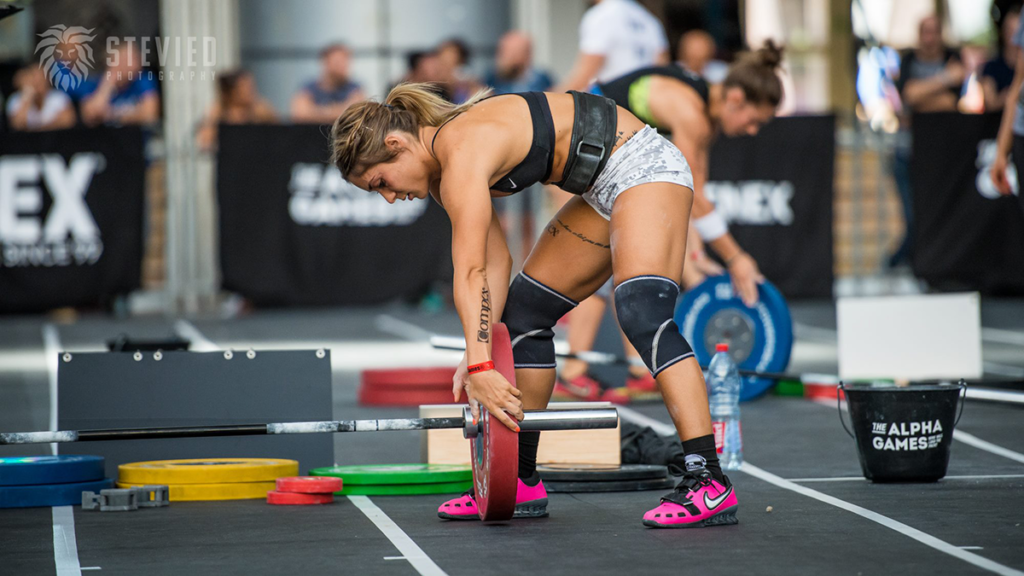 woman in weightlifting shoes loads up barbell during competition