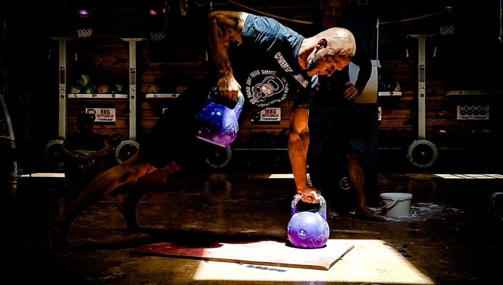 man performs hard kettlebell workout with gorilla cleans