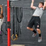 two teenagers practice pull ups in a gym