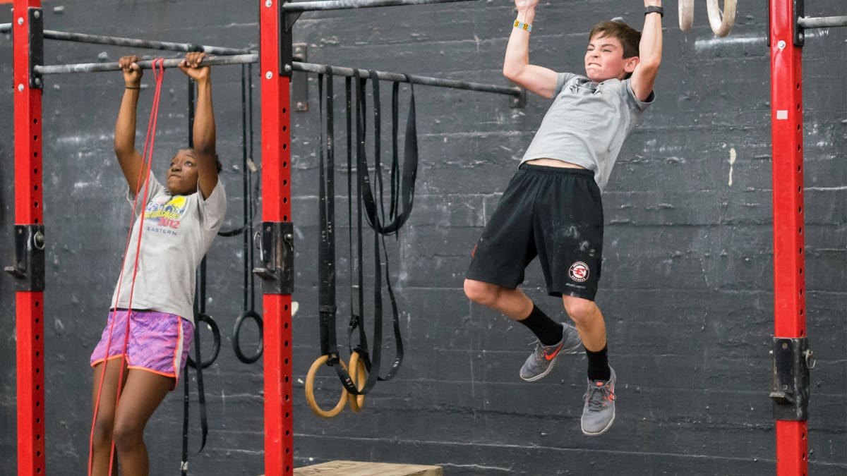 two teenagers practice pull ups in a gym
