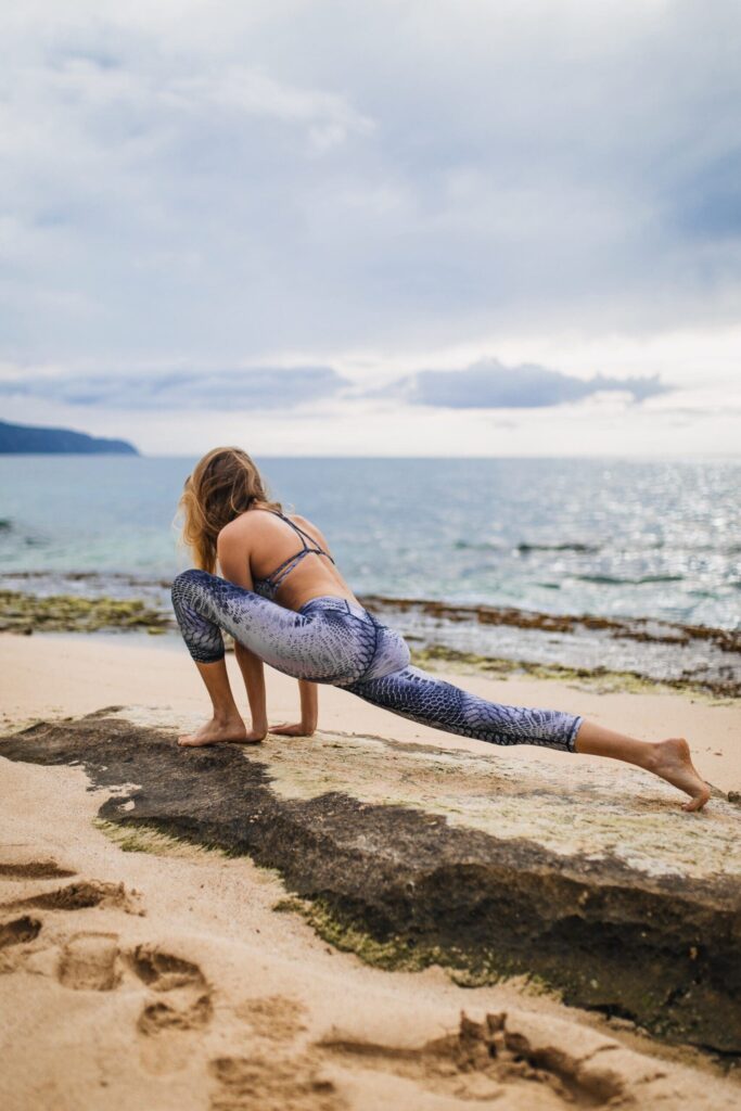 woman does hip opening exercises by the beach