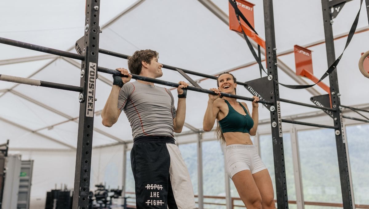 Foto de Sporty fitness couple doing pull up on horizontal bar in gym.  Muscular man and woman pulling up, working out. do Stock